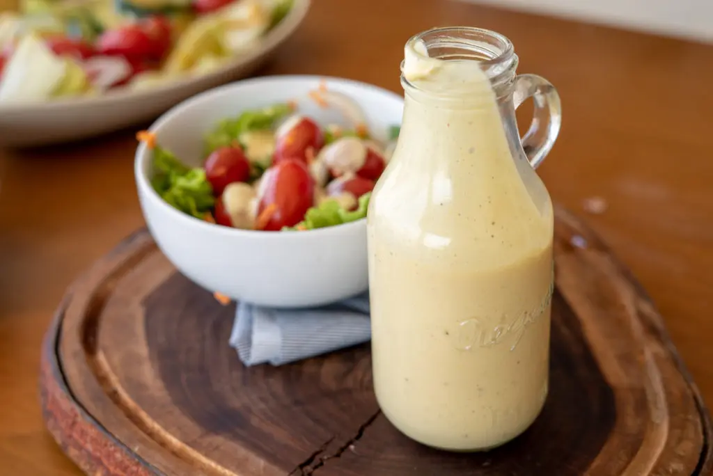 molho mostarda e mel ao lado de um pote branco com salada sobre tábua de madeira