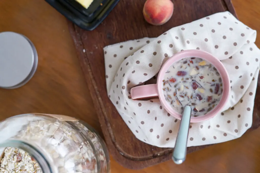 sobre um guardanapo de bolinhas, uma xícara rosa com o mingau de aveia, castanhas e sementes feito com o mix da receita